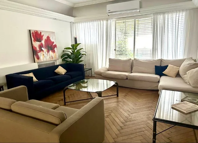 A bright living room with cream and navy sofas, parquet flooring and large windows.