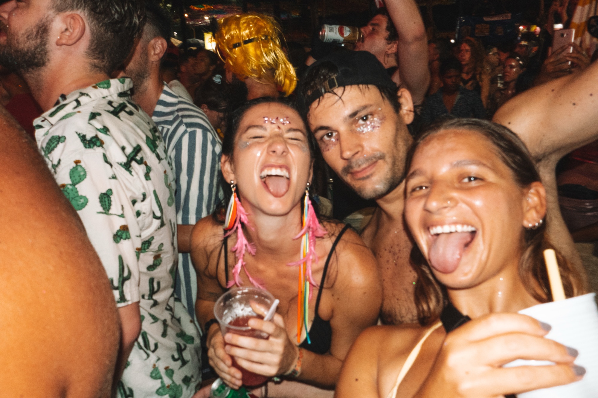 Three Casa Basilico guests in glitter and feather earrings laughing at a night-time Carnival party