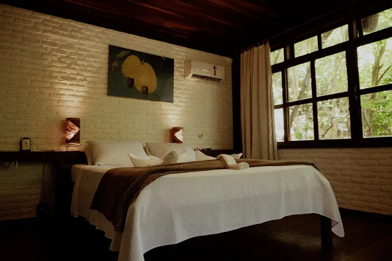 Double bed with a brown throw beneath a painting, beside a large window, inside a Comfort Chalet in Pipa
